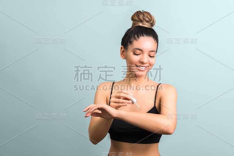 美丽的女人与聚集的头发应用身体油保湿对一个蓝色的背景