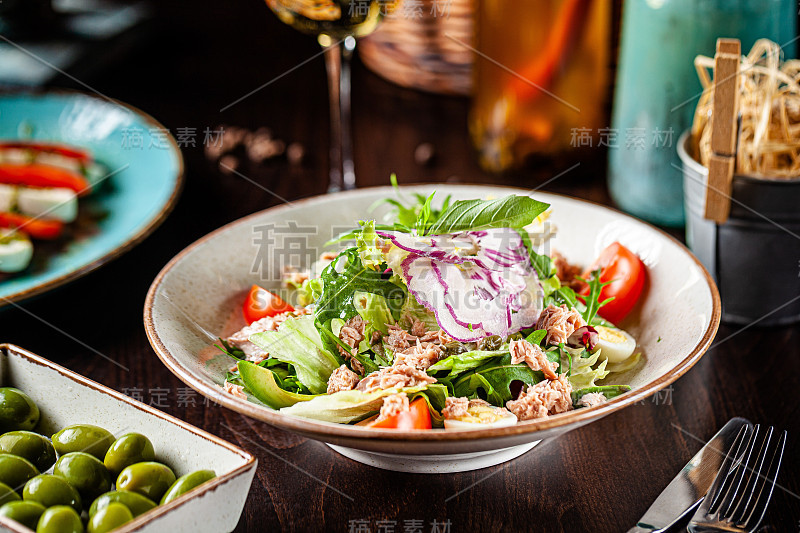 西班牙菜。什锦沙拉，樱桃番茄，鹌鹑蛋，酸豆，牛油果，芝麻菜，金枪鱼。在餐馆里用白盘子上菜。背景图像，