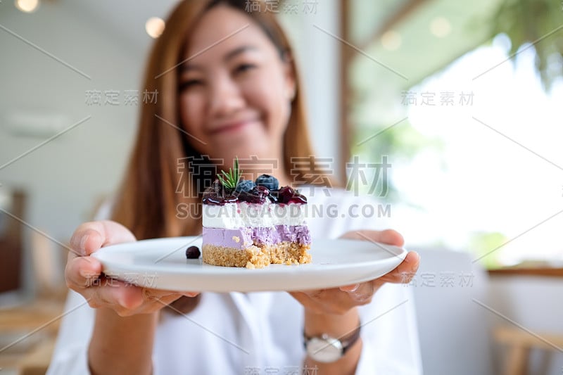 一位年轻美丽的亚洲女子拿着一盘蓝莓芝士蛋糕