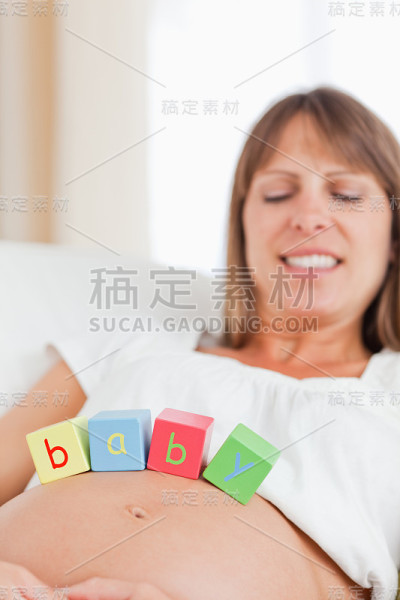 迷人的孕妇躺在沙发上玩积木