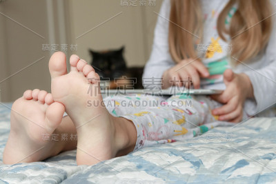 穿着睡衣的女孩坐在床上玩平板电脑