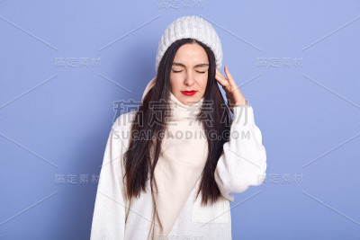 水平图片的年轻迷人的女人站孤立在工作室的蓝色背景，把手放在耳朵上，有耳朵疼，有感冒，闭上眼睛，穿着白