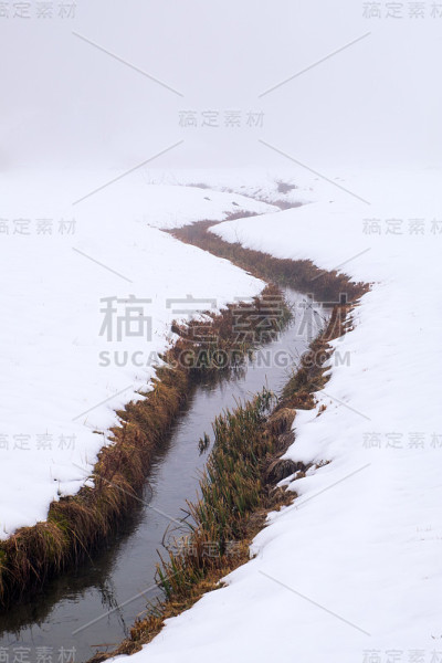 河岸上灌木丛生的小河蜿蜒穿过白雪皑皑的田野