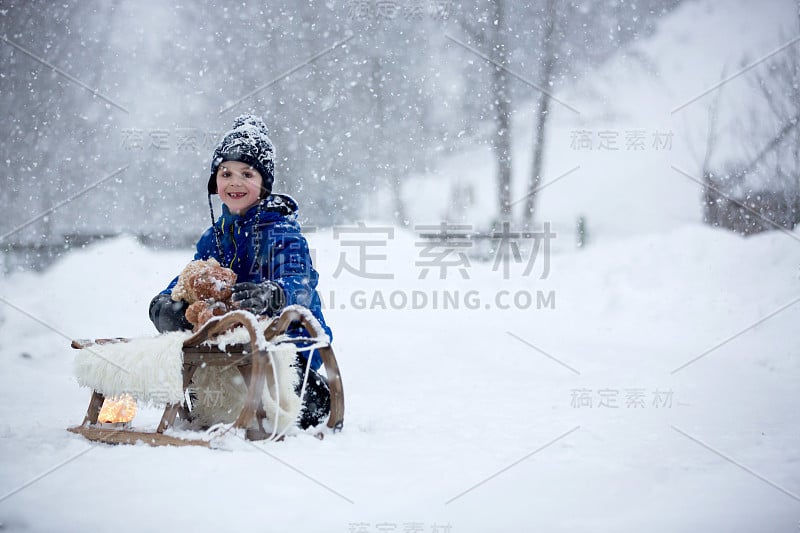 可爱的男孩在雪地里玩泰迪熊，冬天的时候。小孩子在下雪天玩玩具