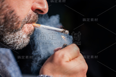 近距离的胡子男子拿着打火机和吸烟的黑色背景。