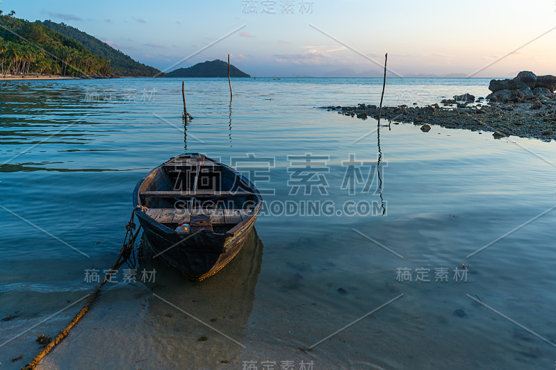 热带岛屿海岸外的木船。傍晚，夕阳在海上。热带景观。光波摇动船