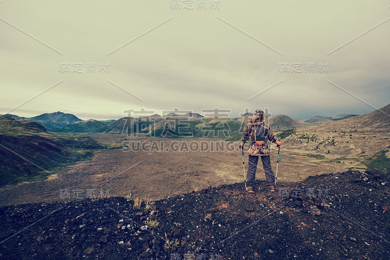 女士徒步背包站在山顶，从火山山顶到冰冻的熔岩山谷