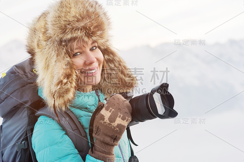 一个快乐微笑的女孩旅行者在一个大的毛皮帽子和编织的手套与相机在他的手的特写肖像