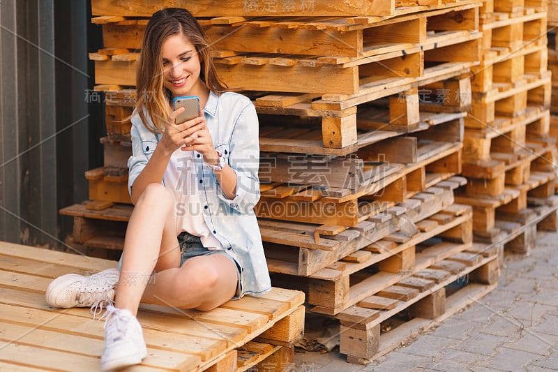 一个微笑的年轻随意的漂亮女人看手机的肖像