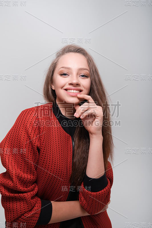 这是一个年轻美丽的女孩的特写，她有着蓝色的眼睛和棕色的头发，穿着黑色t恤和红色短夹克