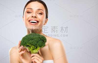 美丽，年轻的女人手里拿着新鲜，绿色的花椰菜。露齿的微笑和闪亮的面部表情。