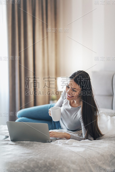 女孩躺在床上喝咖啡，用笔记本电脑。