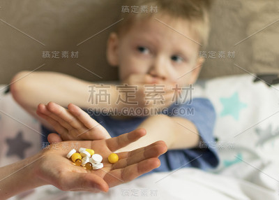 一个生病的伤心的孩子，因为发烧和头痛躺在床上，拒绝服药和药片。流感及感冒病毒