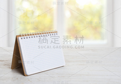在模糊的窗户背景上放在木桌上的记事本或日历