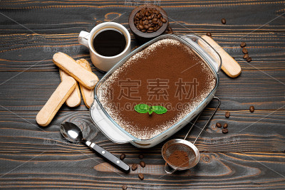 传统的意大利提拉米苏甜点在玻璃烤盘，savoiardi饼干和一杯新鲜的热咖啡在木背景