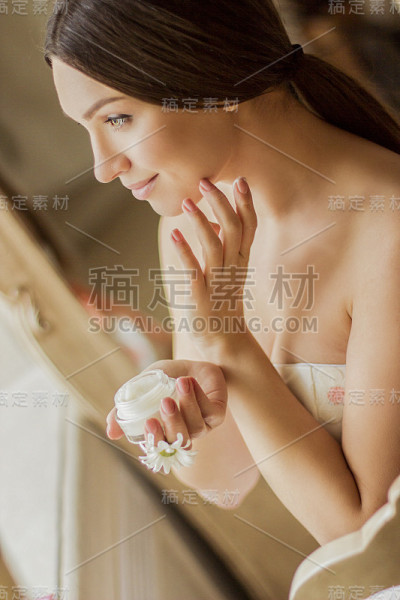 女人透过窗户往脸上涂保湿霜