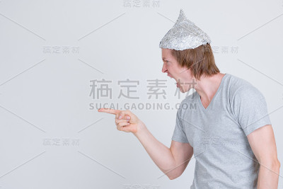 侧面视图的压力年轻男子与锡纸帽指着手指，看起来生气