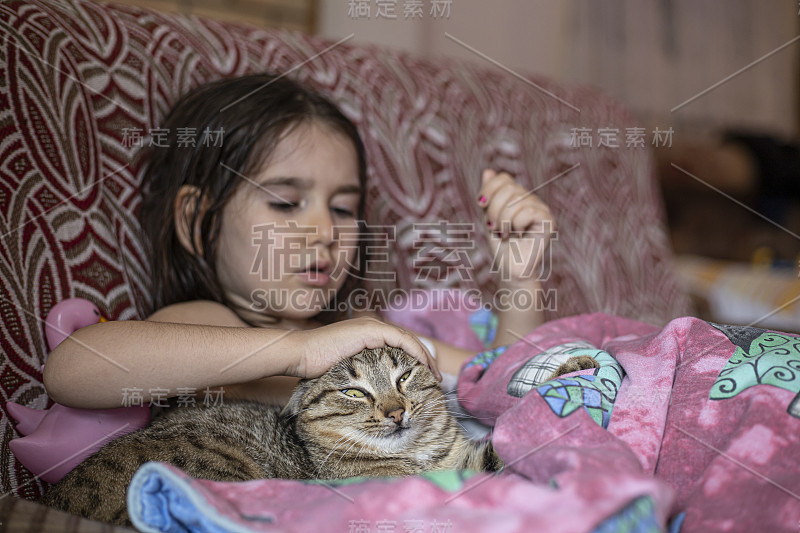 小女孩裹着毯子，在沙发上抚摸着她的宠物猫