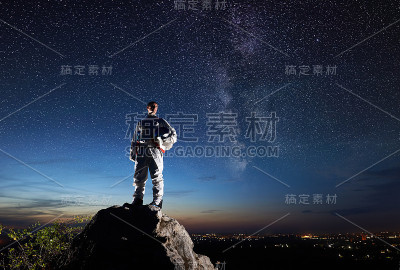 宇航员站在岩石山在夜空下繁星点点。