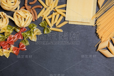 不同类型的意大利面在黑色石板背景与复制空间。俯视图