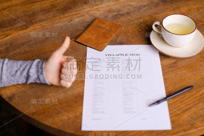 咖啡馆桌上放着签证申请表和护照，竖起大拇指