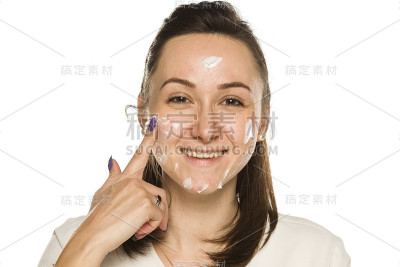 年轻女子微笑着在白底的脸上涂上了面霜