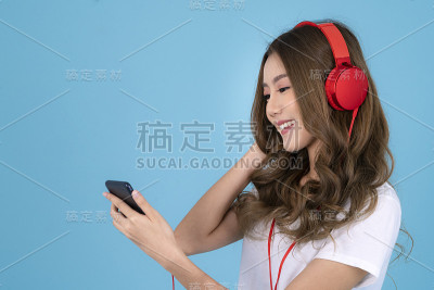 亚洲女性戴着耳机，在蓝色的孤立背景下听音乐