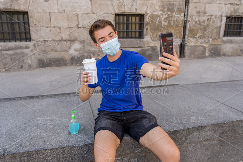 一名年轻人在城市街道上戴着防护口罩，用洗手液和视频给朋友和家人打电话。保持联系，遏制疫情传播，遏制新