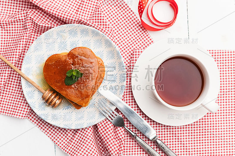 在明亮的背景上放着心形的煎饼。情人节的节日早餐或给爱人的惊喜的概念