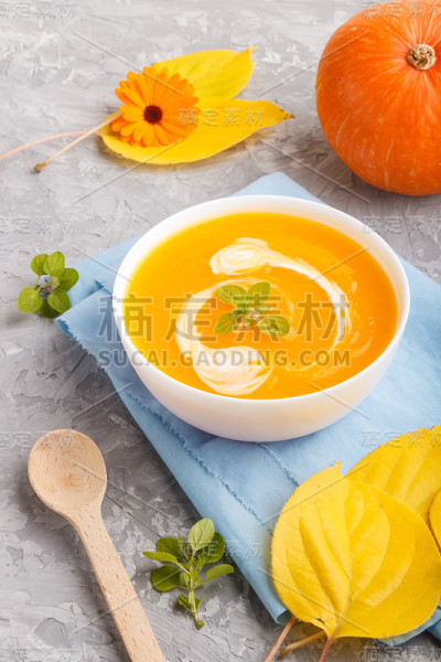 传统的南瓜奶油汤，白色的碗，灰色的混凝土背景和蓝色的餐巾。侧视图，特写。