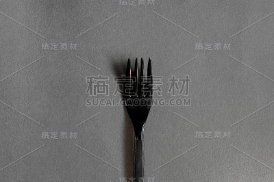 简单干净的黑色塑料叉子在一个平坦干净的灰色背景与硬阴影。极简主义单色照片的菜肴。