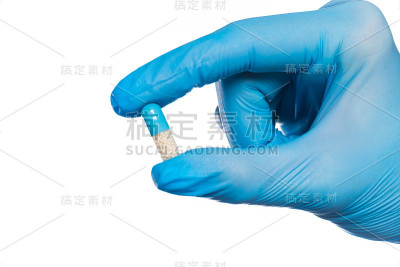 外科医生的手戴着蓝色医用手套，手上有一个孤立的白色药丸泡