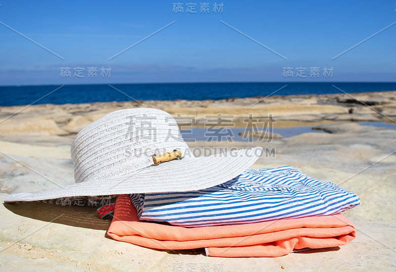 假日度假夏日海滩背景。以蓝色大海为背景的沙滩上的帽子和地毯