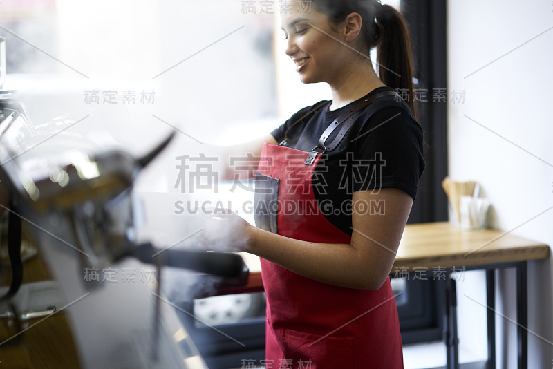 身着制服的女服务员兴高采烈地站在吧台边，在机器上煮咖啡，心情舒畅地上菜。美丽的女店主零售业务作为咖啡