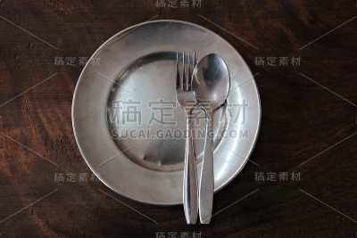黑色的木桌上放着干净的圆形不锈钢盘子和勺子。拷贝空间的俯视图。