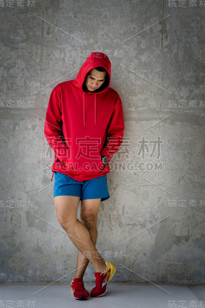 亚洲人穿着运动服和帽衫站在户外垃圾墙。