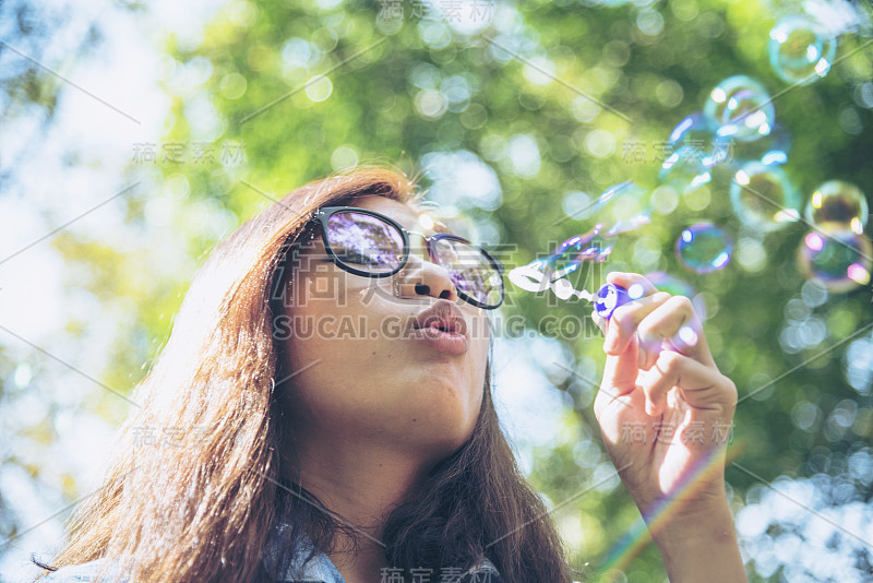 可爱的快乐可爱的女孩顽皮的泡沫泡沫在绿色的操场在夏天的户外。快乐的女孩在公园里快乐的时光。泡泡吹肥皂