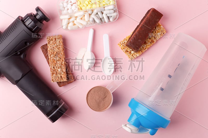 治疗撞击按摩枪，fit meal，药丸，运动能量棒在粉红色的背景-现代体育活动和饮食的概念，健康生活