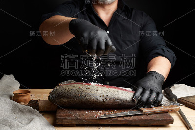 厨师穿着黑色衬衫和黑色乳胶手套准备鲑鱼片