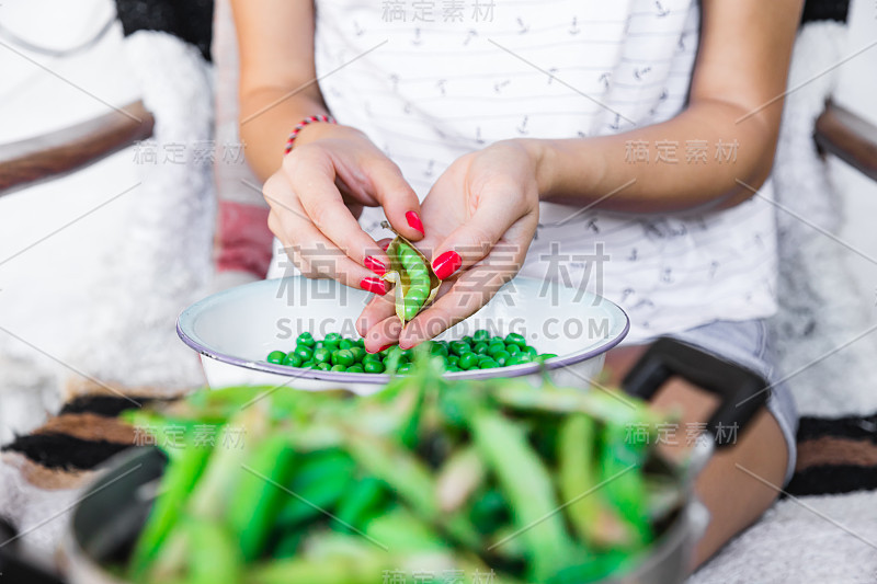 一名妇女正在准备新鲜的有机豌豆，并将其从壳中取出。