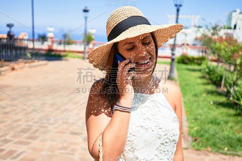 年轻美丽的女人微笑着快乐地走在城市的街道上，在一个阳光明媚的日子里，用智能手机打电话