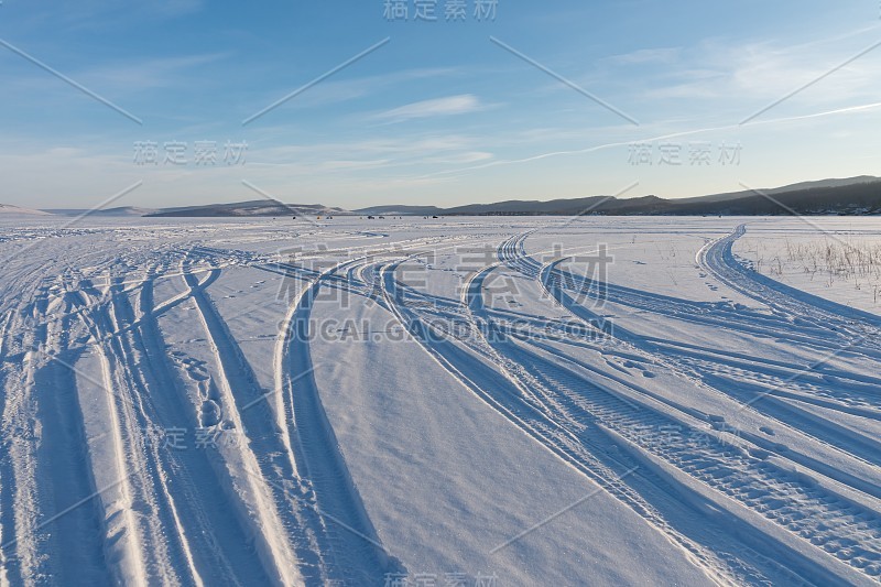 汽车的痕迹沿着结冰的大湖的白雪延伸到远处。