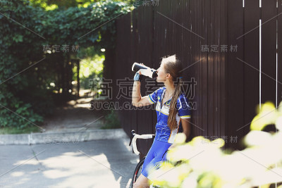 渴。女自行车手在自行车附近喝水