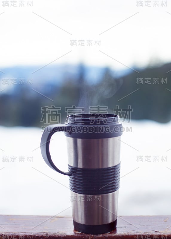 金属杯和热气腾腾的咖啡在山和雪的背景