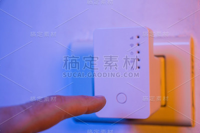 男子将手指按在WiFi中继器的WPS按钮上，该按钮位于墙上的电源插座上