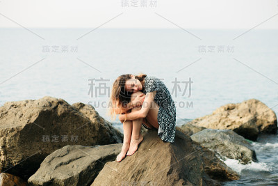 一个年轻美丽的女孩穿着大石头，风景如画的海边