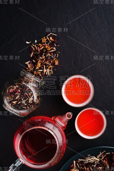 两碗，玻璃茶壶，玻璃罐和盘子，在黑色的混凝土背景上的干茶叶清香的新鲜冲泡的天然红果茶