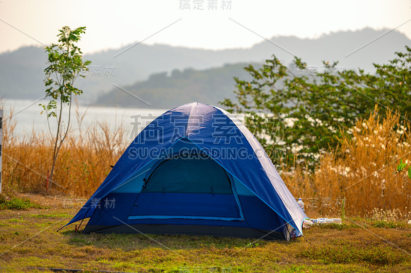 蓝色帐篷放置在有山有水的森林中间。