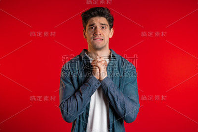 英俊的男子在衬衫祈祷在红色的背景。一个欧洲人在乞求某个人。