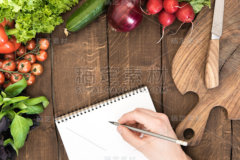 食物组成生蔬菜，切菜板和人的手能在记事本上写东西的木制背景